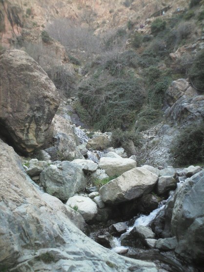 Narrow gorge with stream skipping around boulders and some vegetation on the rocks.