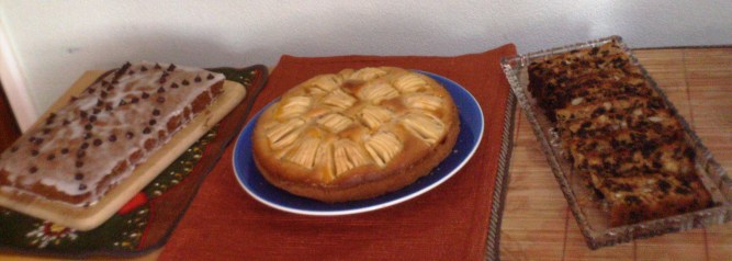 Three cakes: one glazed and decorated, one topped with fresh fruit in a pattern, one with plenty of dried fruits and nuts.