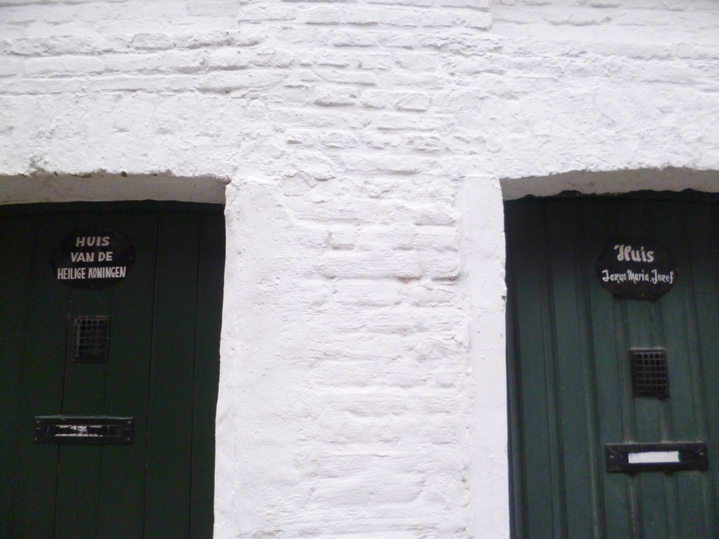 Two heavy black wooden doors in a white brick wall, with inscriptions as below.