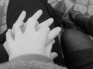 Black & white photo: Intertwined hands of a woman and a man; below, their shoes.